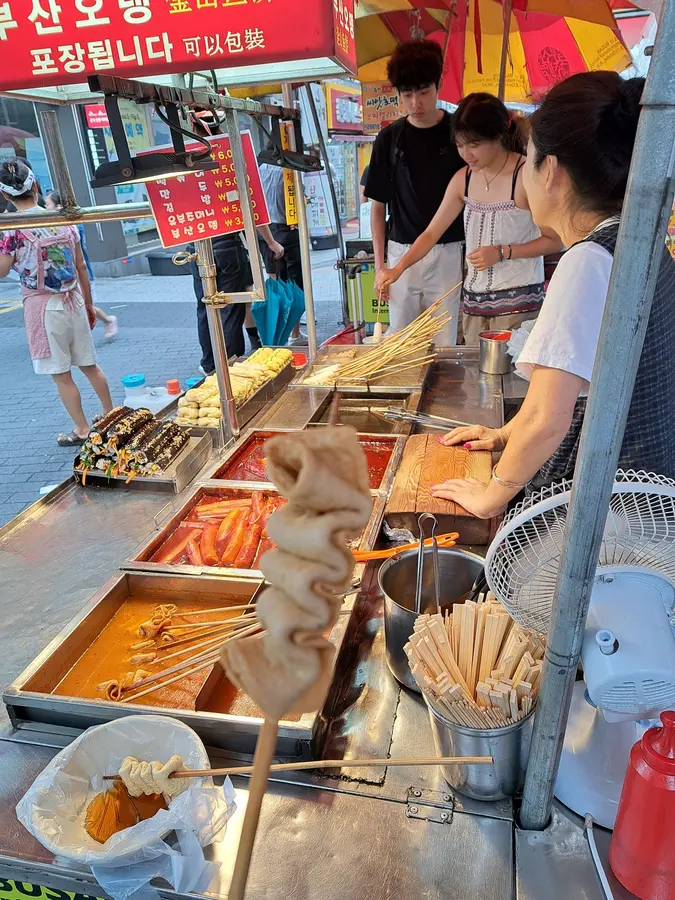 Ein Strassenstand, wo Reiskuchen in scharfer Sauce (Tteokbokki), Fish cakes (Eomuk - sehr lecker) und Gimbap-Rollen (sozusagen koreanische Sushirollen) verkauft werden.