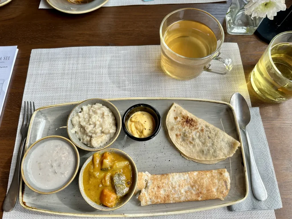 Frühstück: Porridge, Gekochte Banane in Kokosmilch, Kokos-Chutney mit einem Dosa und ein mit Mungbohnen-Zucker-Anis-Gemisch gefüllten Crèpe